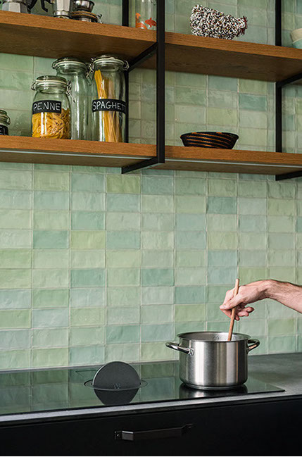 Man cooking in a modern kitchen with green tile backsplash and black cabinets.