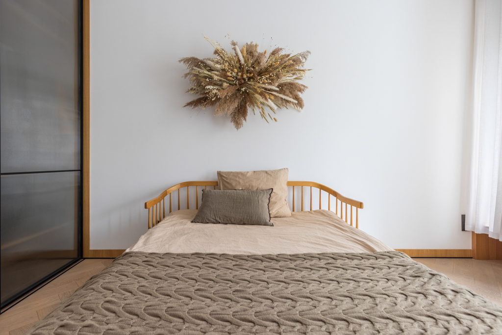 Minimalist bedroom with natural wooden bed frame and dried floral arrangement above the bed.