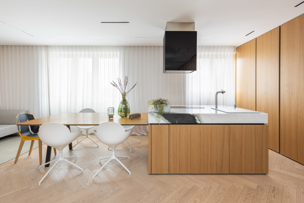 Minimalist kitchen with wood cabinetry and white chairs in a modern Berlin apartment.