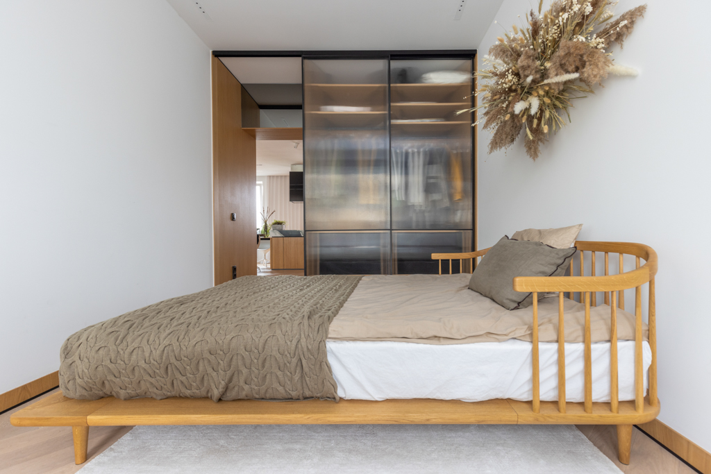 Minimalist bedroom with natural wooden bed frame and dried floral arrangement above the bed.